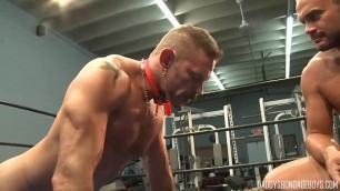 Studly man with an electro collar on is tied up and told to do push-ups